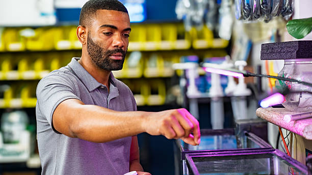 istock Man feeding fish in aquarium at pet store with shelving background — medium shot during daytime 2232764015