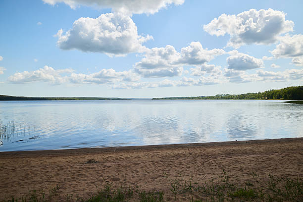 A peaceful view of a lake with stunning reflections, sandy beach, and fluffy clouds under a bright blue sky