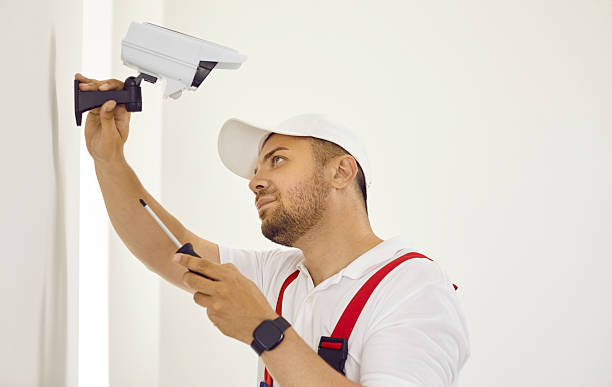 istock Concentrated male installer is using screwdriver to mount CCTV camera on white wall. 2232775866