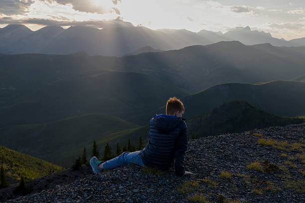 istock Boy watches sunset over mountain ridge 2232776941