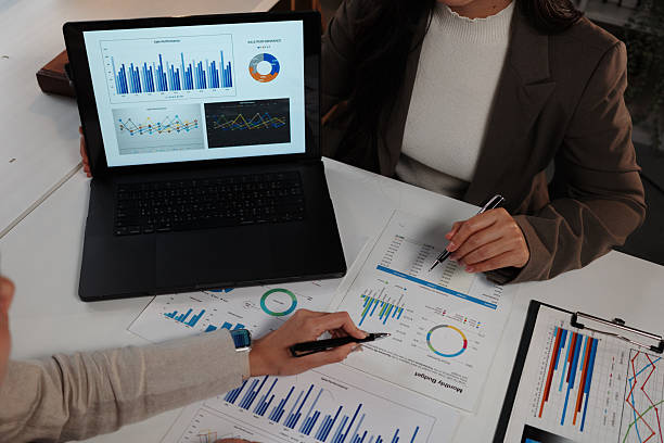 istock Professional women reviewing financial data, discussing project details while examining charts, graphs, laptop screen, and printed reports at shared workspace 2232781581