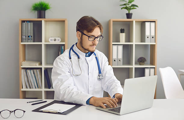 istock Doctor sitting at table and working with electronic medical records on laptop computer 2232783838