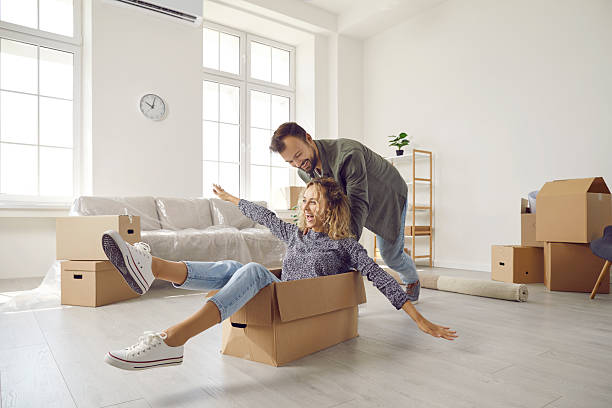 istock Happy young married couple having fun using cardboard boxes in new home on moving day. 2232786482