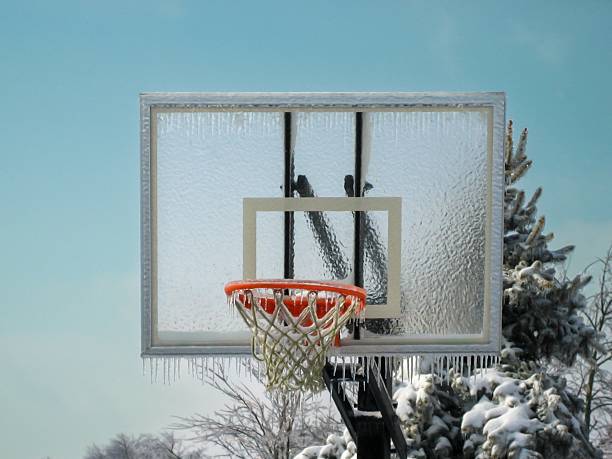 Basketball goal with glass backboard in winter showing ice buildup on goal, net and backboard as well as icicles.