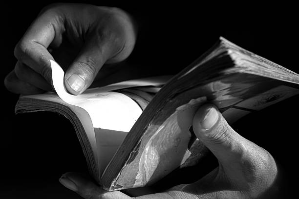 istock Hand of person reading a book against low light background 2232788653