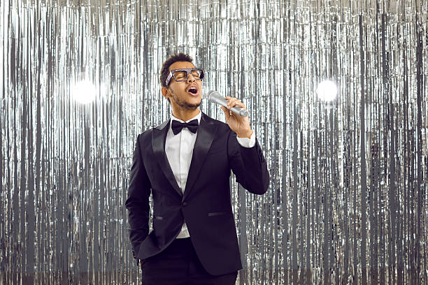 istock Young black singer in tuxedo suit standing on stage, holding microphone and singing 2232799109
