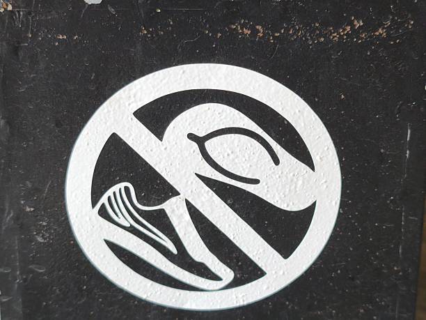A white circular prohibition sign on a textured black background, featuring symbols of a shoe and a fruit crossed out, indicating restricted actions.
