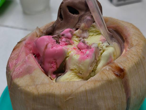 Scoops of colorful strawberry, vanilla, and chocolate ice cream are served inside a refreshing young coconut shell, with a spoon ready to enjoy this tropical dessert.