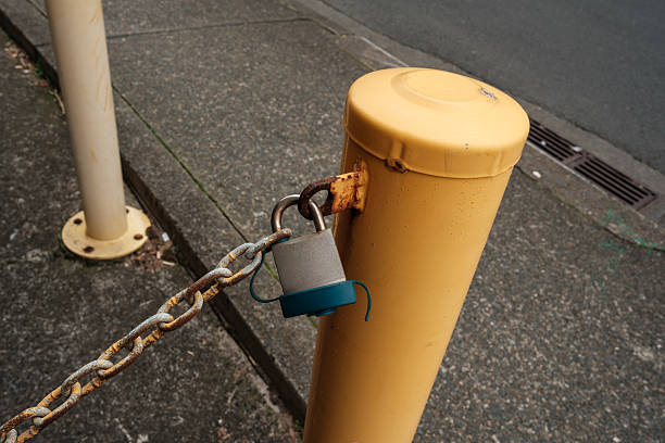 Rusty metal chain blocking an empty roadway. Outdoor barrier with warning reflectors. White road markings on asphalt. Estricted access and closed passage