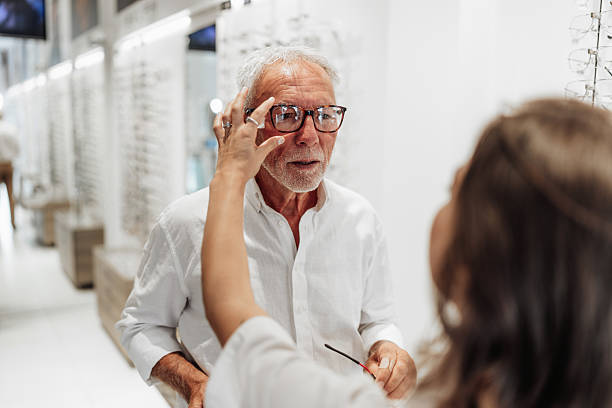 Senior man trying eyeglasses with optician in optical store