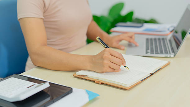 istock Woman writing notebook, working at desk with laptop, calculator, documents, focused mood 2232808711