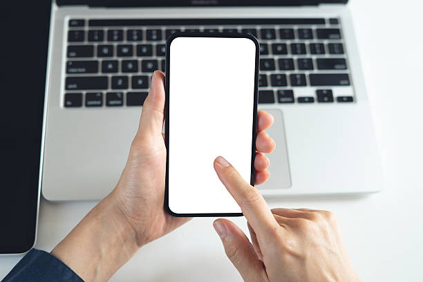istock Blank white screen cell phone mockup. Close up, business person using smartphone, finger touching on screen during working on laptop computer on office table, empty space for social media marketing or mobile app design, overhead shot 2232809039
