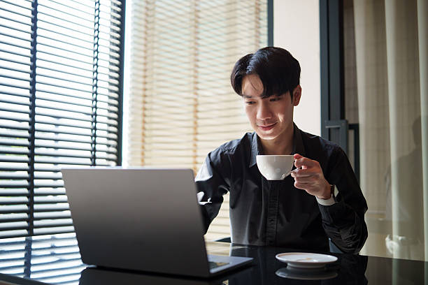 istock Young businessman working on laptop while enjoying a hot drink, sitting in a modern office. 2232809084