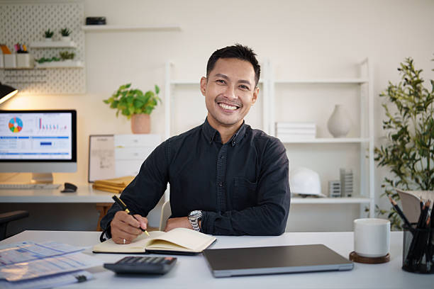 istock onfident young Asian businessman smiling at the camera while working at his desk in a modern office. 2232809410