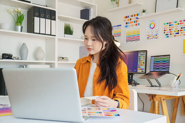 istock Young female graphic designer working on creative projects at desk with a laptop and color samples. 2232810519