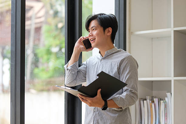 istock Young businessman having a cheerful conversation on his smartphone, standing by a large window. 2232810569