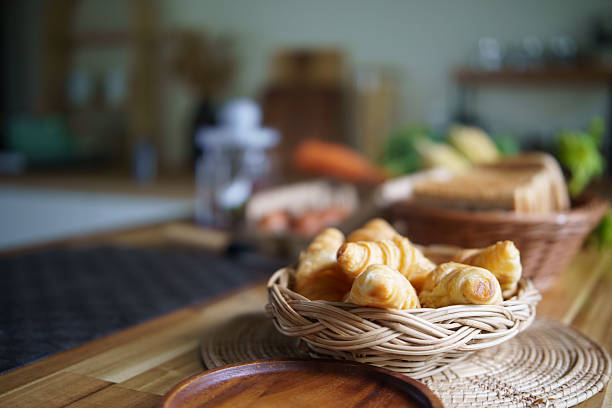 Freshly baked croissants in a wicker basket on a wooden kitchen table.