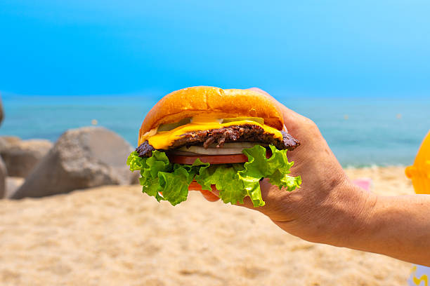 Man holding burger in a hand against beach background