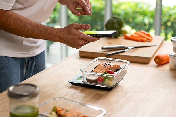 Man using phone while preparing healthy homemade meal prep with fresh food at home.