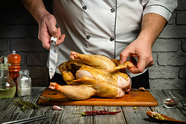 istock A chef skillfully processes a whole chicken on a wooden cutting board. Fresh herbs and spices are arranged beside him, showcasing a commitment to quality culinary preparation 2232821201
