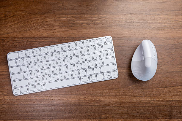 istock Clean modern office setup with white wireless keyboard and ergonomic vertical mouse on wooden desk, promoting comfortable productivity and efficient workflow 2232824770
