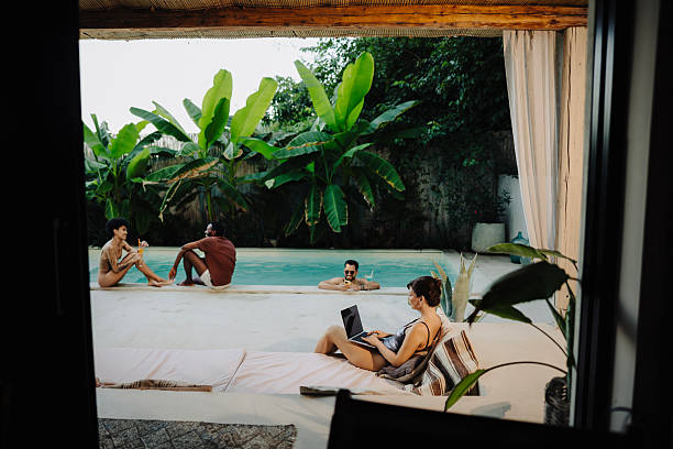 istock Remote work by the pool – woman in swimsuit working on laptop while friends relax 2232828792