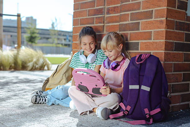 istock Two young girls sharing headphones while using a tablet outdoors 2232833264