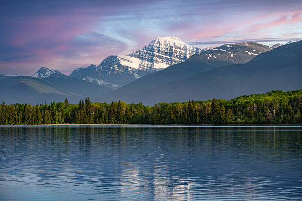 A scenic view of Mount Edith Cavell reflected in a calm lake in Jasper National Park, Alberta, Canada. Snow-capped peaks tower above green forests and shimmering waters, creating a tranquil and iconic Canadian Rockies landscape. This image symbolizes Canada travel, adventure, and pristine wilderness, making it ideal for global buyers seeking nature and exploration themes.