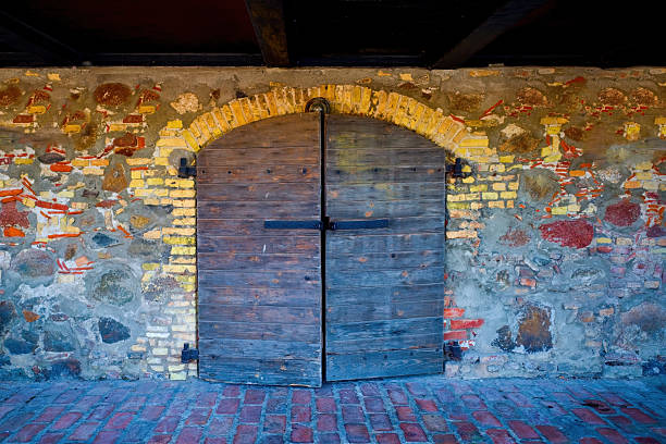 Rustic wooden arched door with iron hinges in a red brick wall at a castle in Western Cape, South Africa.