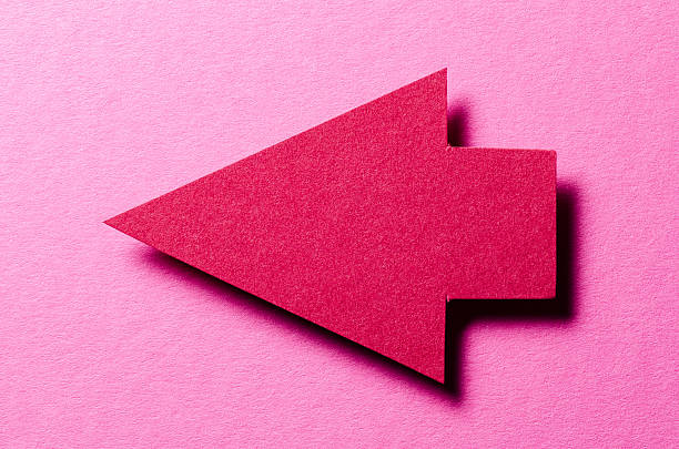 Red cut out blank paper cardboard arrow direction sign with copy space for text on pink background, flat lay top view pointing symbol message backdrop