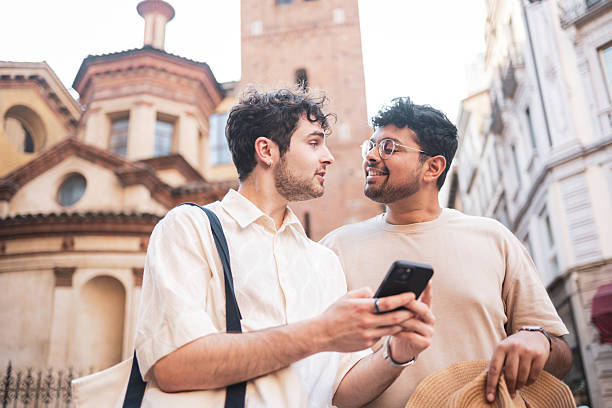 Two male tourists are using a smartphone to explore the city of bologna, italy, standing in front of the santo stefano complex