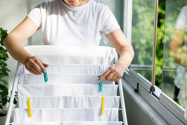 Young woman placing clean wet laundry on drying rack on the balcony of the home