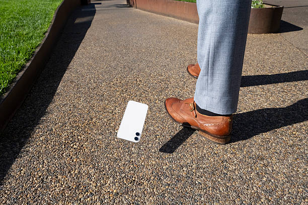 Businessman is about to step on his dropped smartphone on a sidewalk