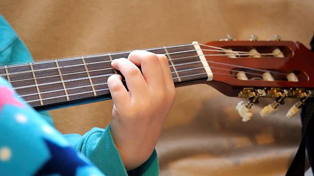 istock Child's hand pressing strings on classical acoustic guitar neck during home practice, closeup view of fingers forming a chord on wooden fretboard, music education and instrument learning concept 2232851809
