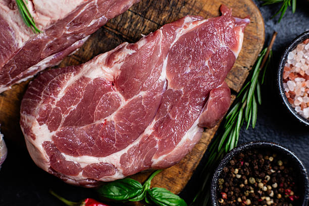 istock Raw pork cuts on a wooden board with herbs and tomatoes, ready to be cooked 2232852657