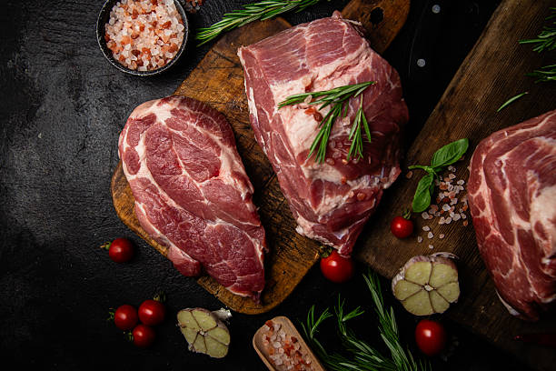 istock Raw pork cuts on a wooden board with herbs and tomatoes, ready to be cooked 2232852866