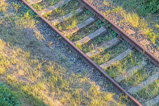 istock Two sets of rusty railroad tracks intersecting at an angle under a clear sky, with scattered vegetation and small rocks in the surrounding landscape Perspective emphasizes depth and light, creating 2232855896