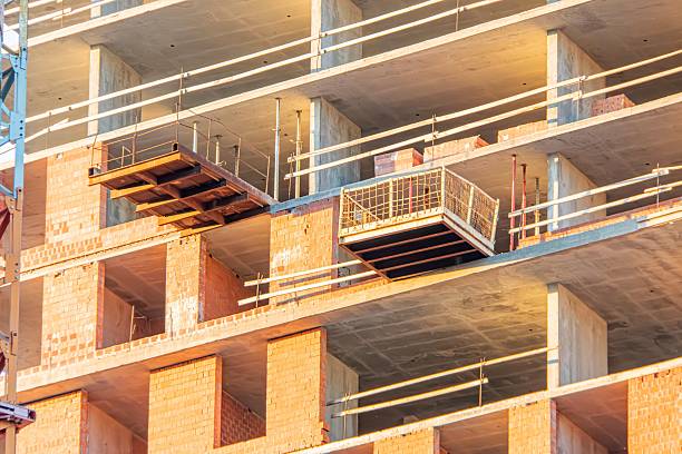 Construction site under sunset, exposed concrete metal beams, unfinished brick wall, scattered construction materials, long shadows, interplay of light shadow, late afternoonearly evening