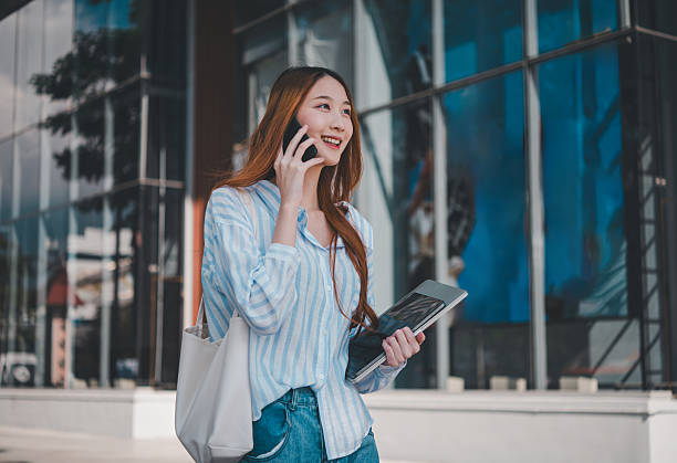 istock A woman is talking on her cell phone while holding a laptop and a handbag 2232856365