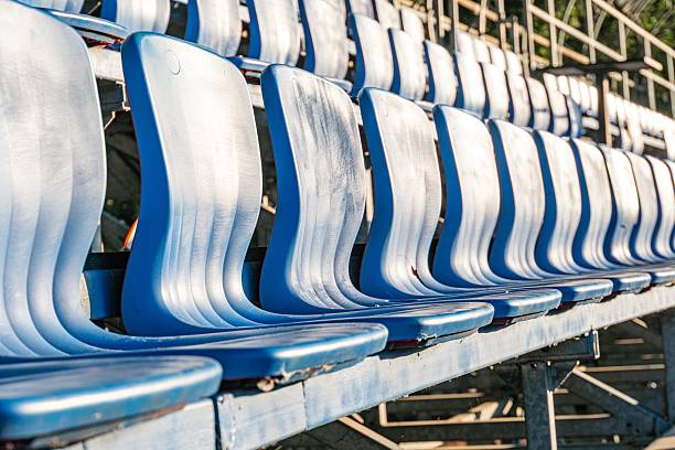 istock Empty blue stadium seats in a row, ascending order, simple design, no armrests or cup holders, gray metal frame, daylight lighting, functional style 2232857273