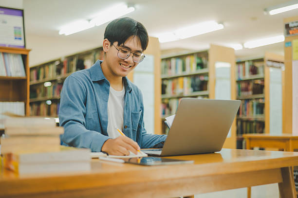 istock Male college students are working on laptops and searching for books to study, make reports, find useful information in college room. Concept of reading, learning and intelligence. 2232857448