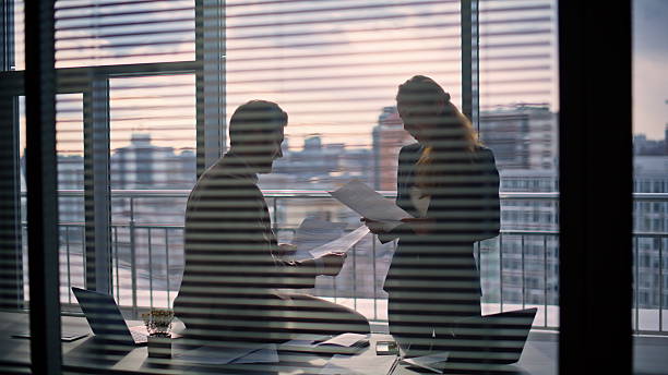 Manager silhouette talking executive reading report at panorama window cabinet