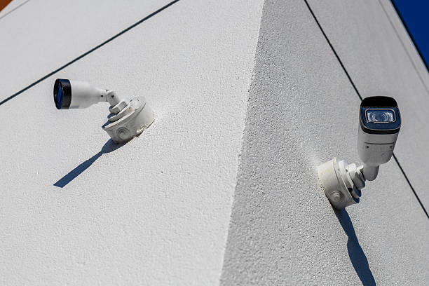 Surveillance cameras are securely installed at the corner of a building, capturing activity under bright daylight