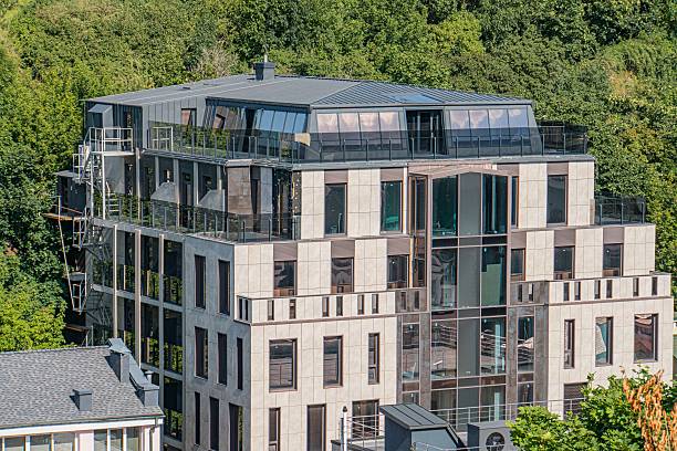 Gray, minimalistic multi-level apartment building with geometric shapes in an urban setting Semi-urban environment with trees in the background Natural daytime lighting