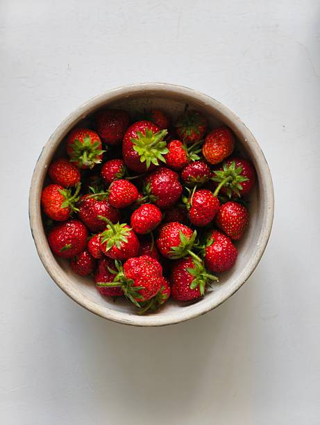 Vibrant red ripe strawberries placed in a bowl against a light white background