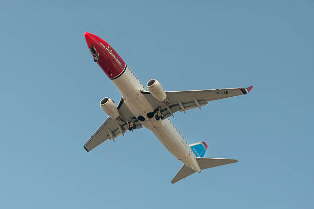 Underside view of a Boeing 737-84P, which is part of the 737-800 series used by Norwegian Air Sweden, with landing gear deployed, set against a clear blue sky. Photographed from below as it came in to land at Rhodes airport in Greece. Built in 2010 it is configured with 189 economy seats and has CFM56-7B26 turbofan engines.