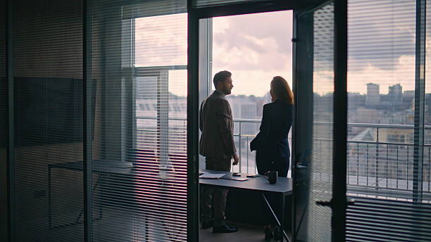 istock Silhouette colleagues talking panorama window office. Relaxed company managers 2232858940