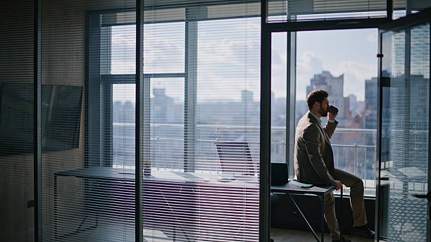 Wealthy businessman enjoying coffee pause sitting office watching large window