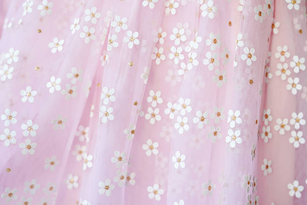 A delicate pink fabric with white daisy flower patterns and golden accents