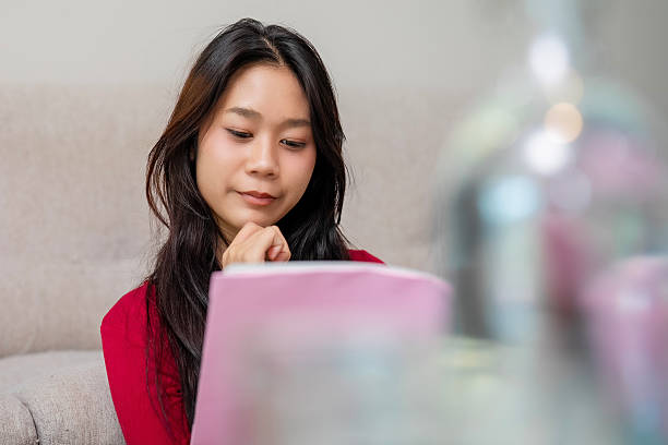 istock Relaxed modern girl with bright smile reading book on sofa, expressing joy, lifestyle, confidence, and the power of knowledge in everyday life. 2232863508